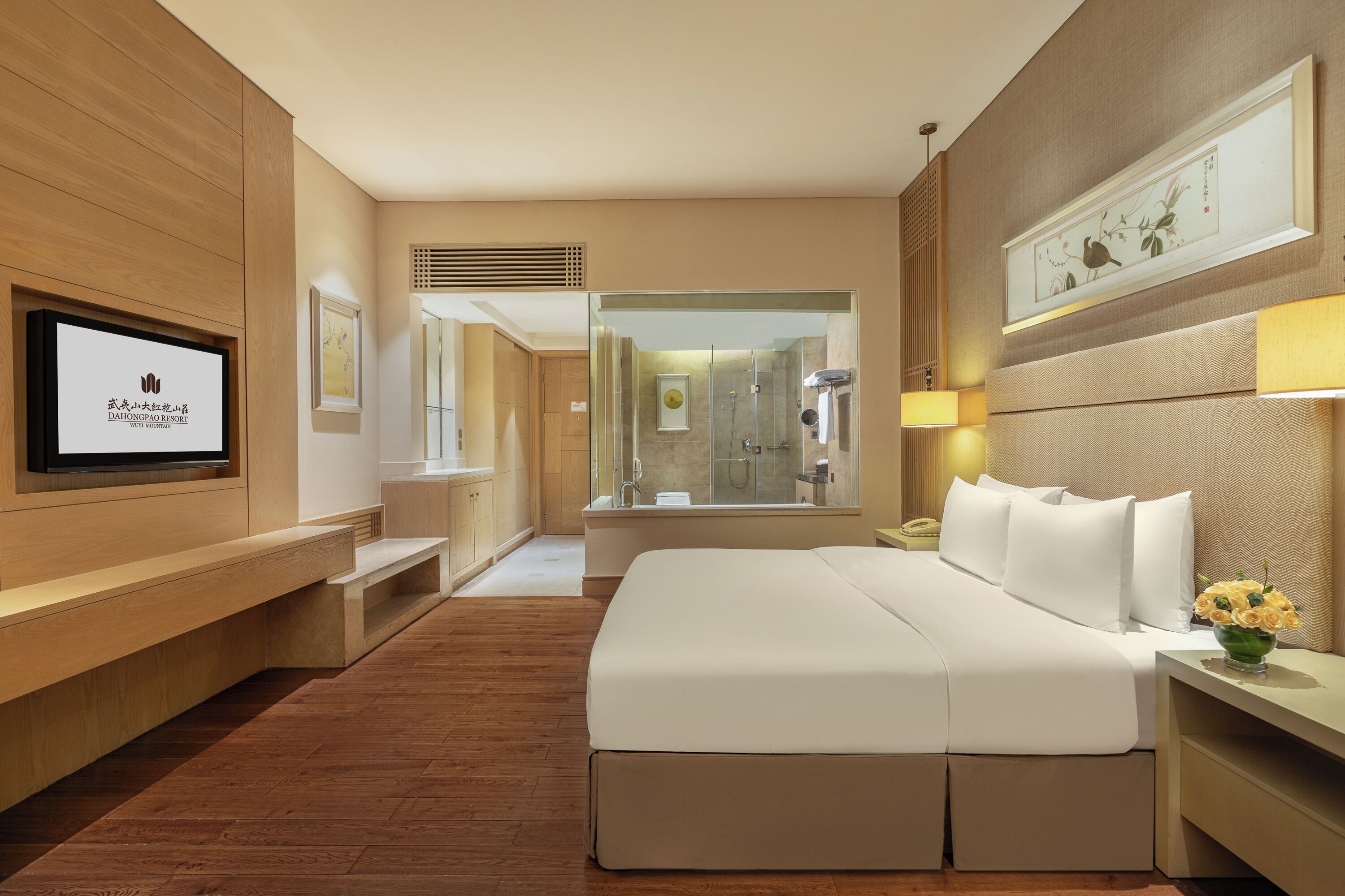 Een hotelkamer met een groot bed, een aan de muur bevestigde televisie, een douche en een houten vloer.