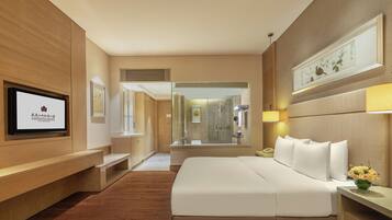 Een hotelkamer met een groot bed, een aan de muur bevestigde televisie, een douche en een houten vloer.