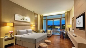 A hotel room with a bed, bedside tables, a TV, a balcony with a view, and a dining area.
