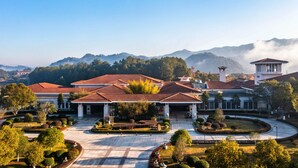 A large building with a red roof, surrounded by well-maintained gardens and a clear view of mountains in the background.