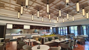 A modern dining area with multiple tables and chairs, a central seating area with a sofa, and a kitchen in the background.