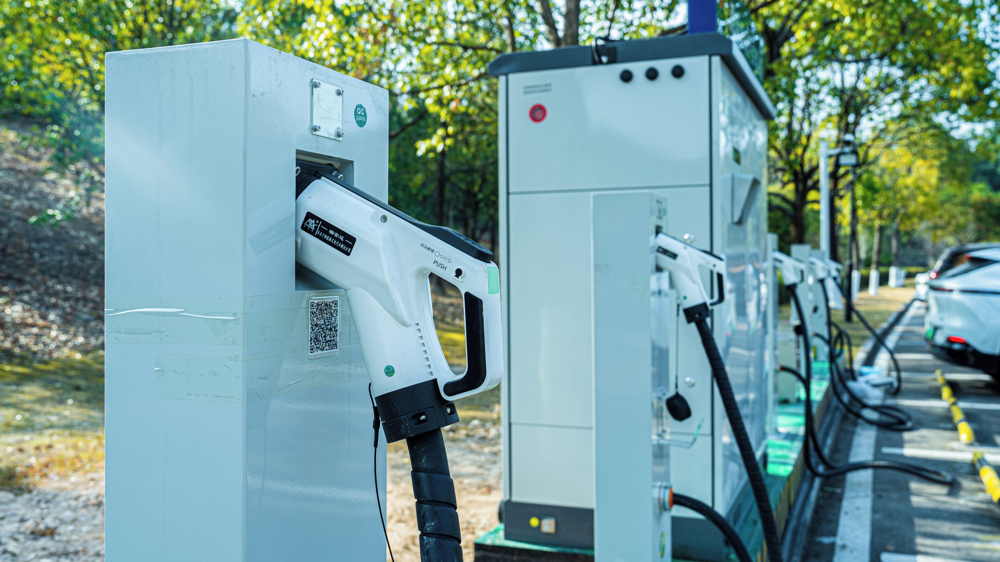 Una fila de estaciones de carga para vehículos eléctricos con códigos QR e instrucciones.