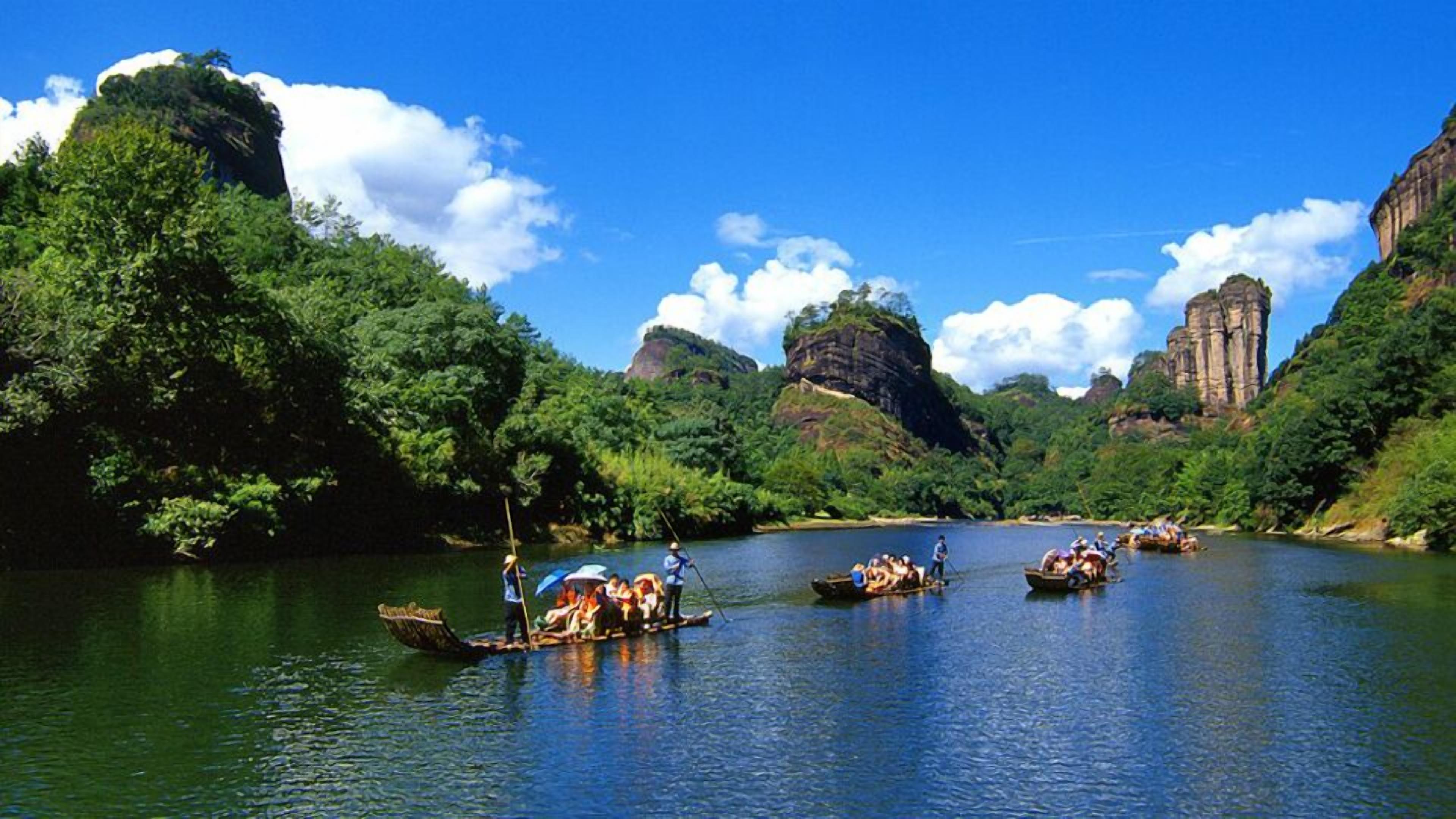 A river with boats and people, surrounded by lush greenery and rocky cliffs.