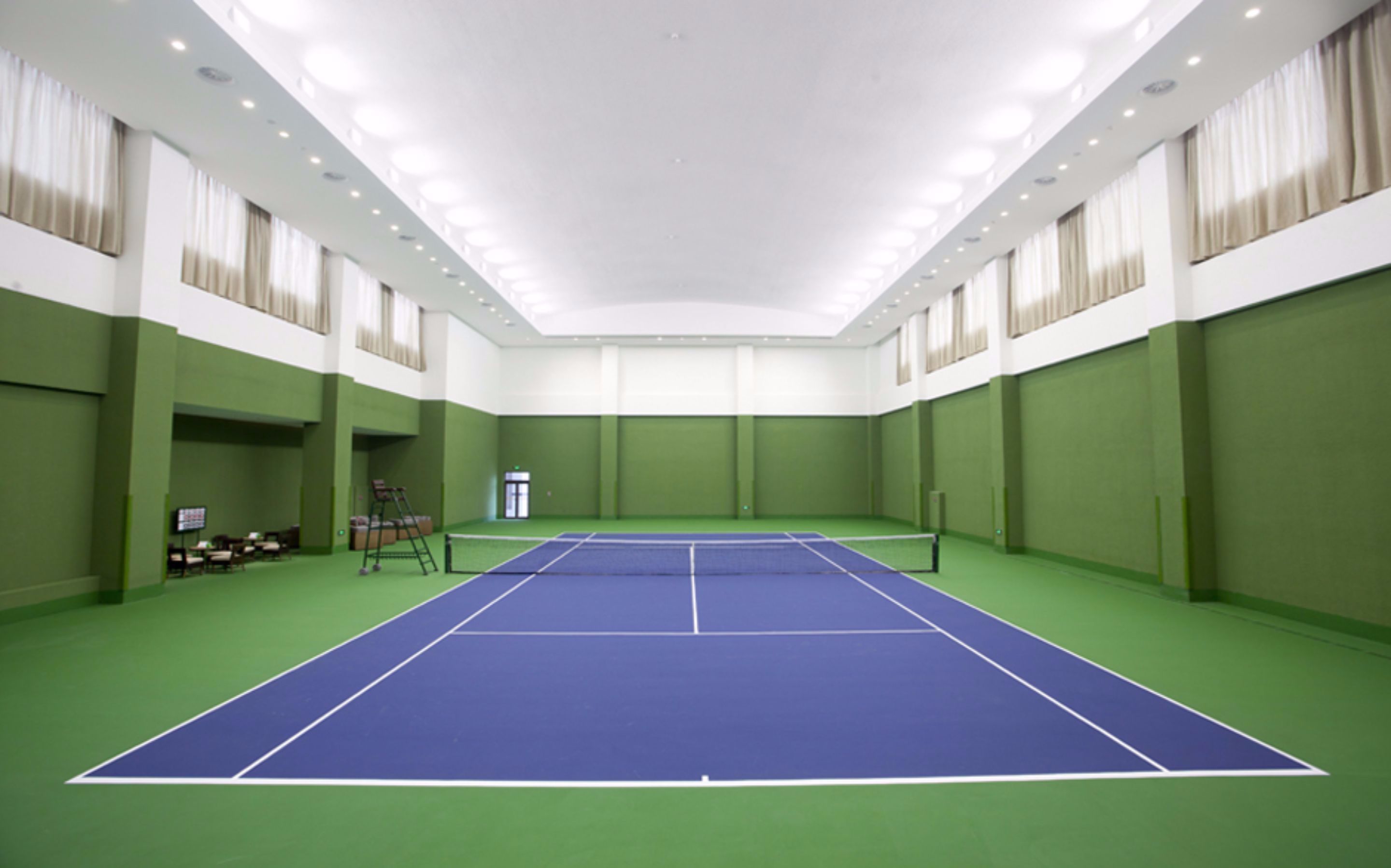 A tennis court with green walls and a blue playing surface.