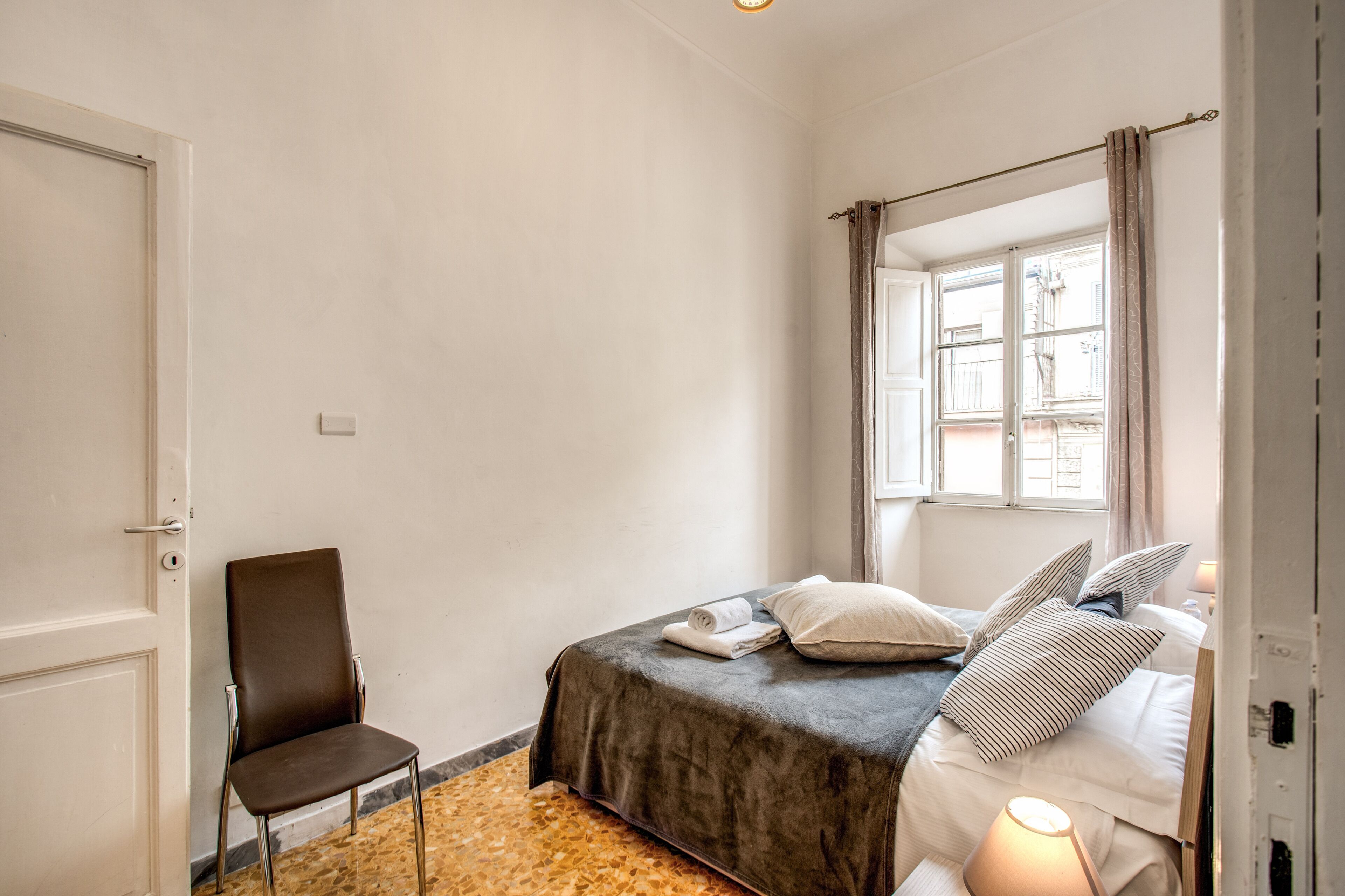 A bedroom with a bed, a chair, a window, and a door.