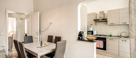 A modern kitchen with a dining area, featuring a checkered floor, a wooden table, and contemporary cabinetry.