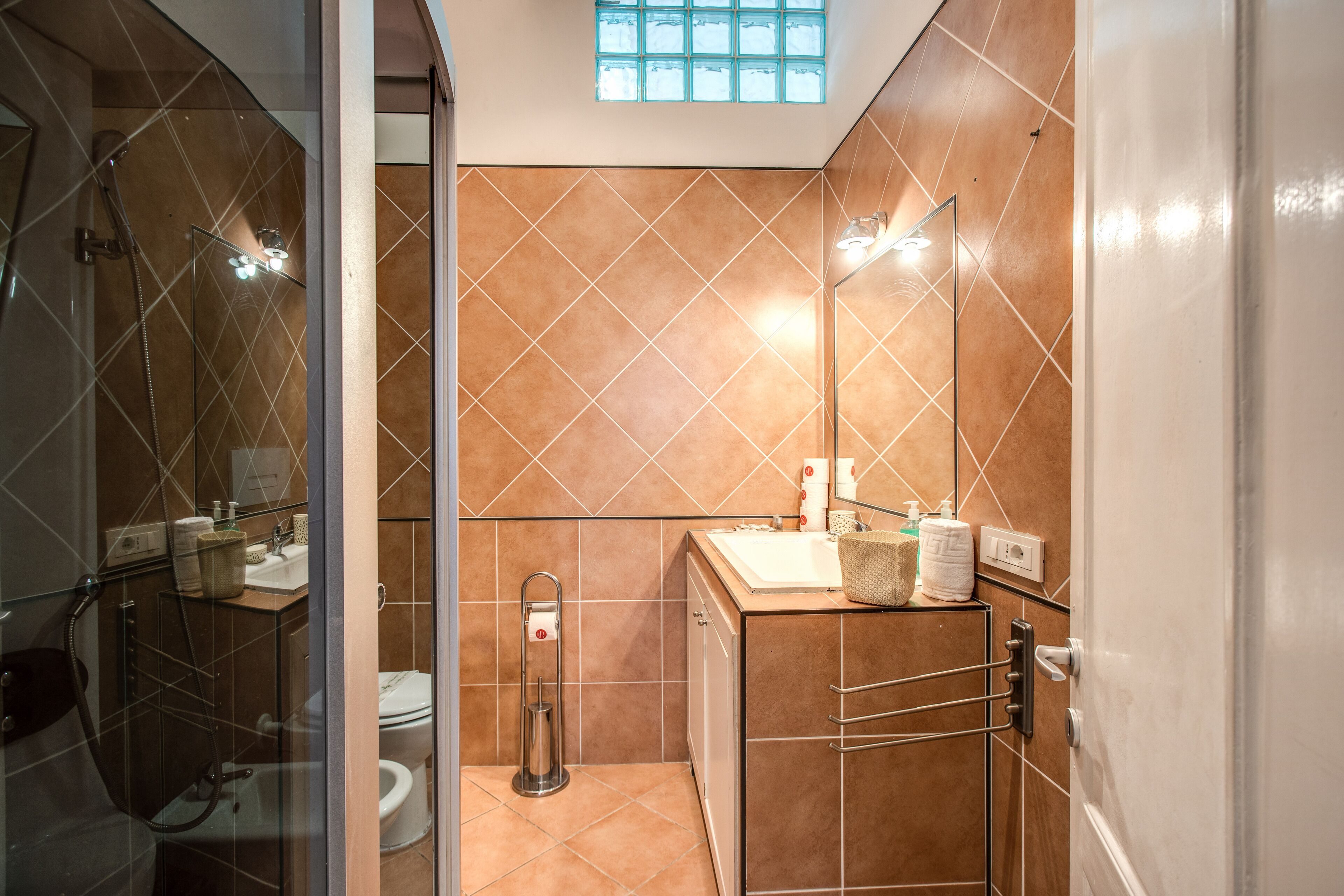 A modern bathroom with a glass shower enclosure, a toilet, and a sink with a towel rack.