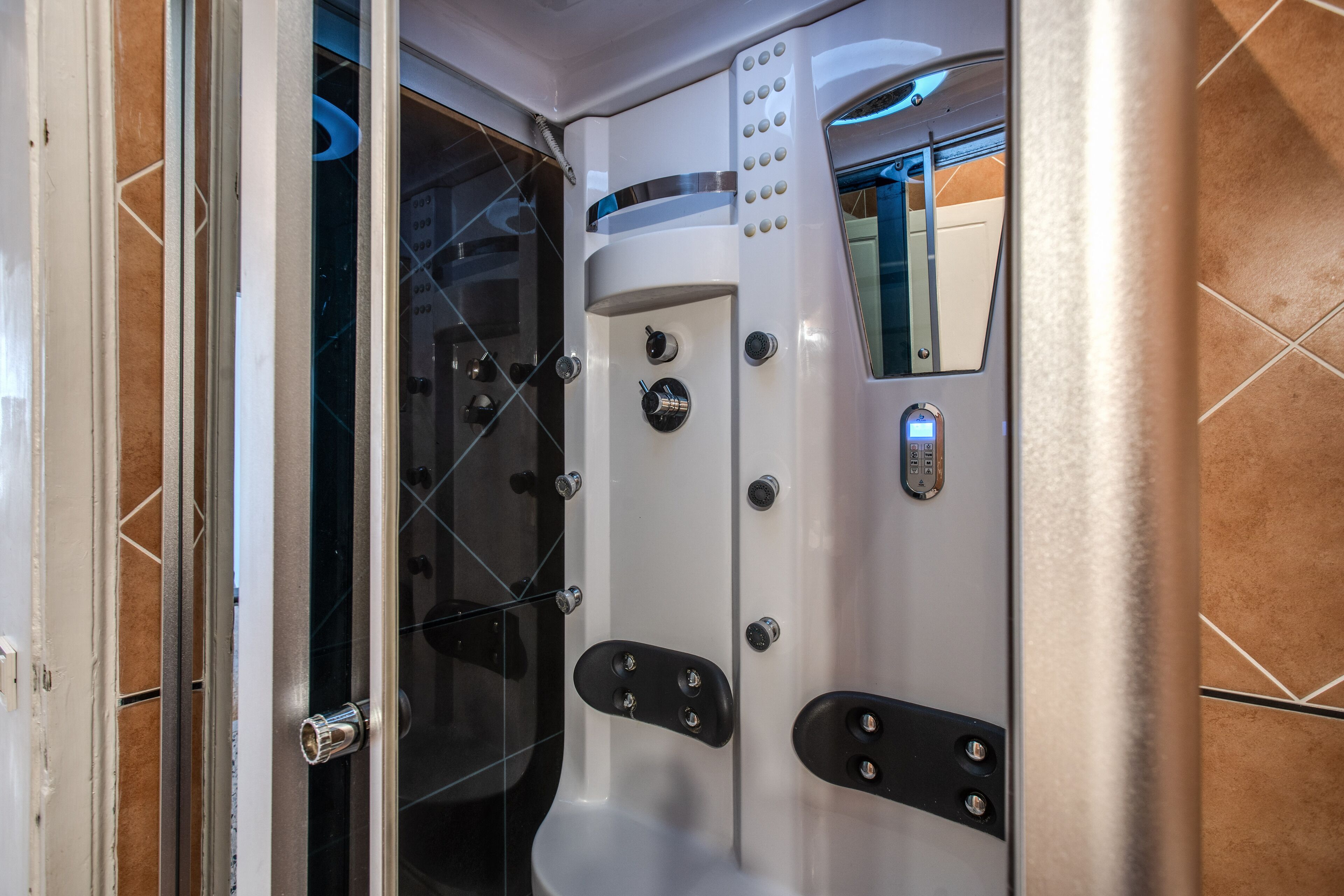 A modern bathroom with a glass shower enclosure, a white bathtub with control knobs, and a mirror.