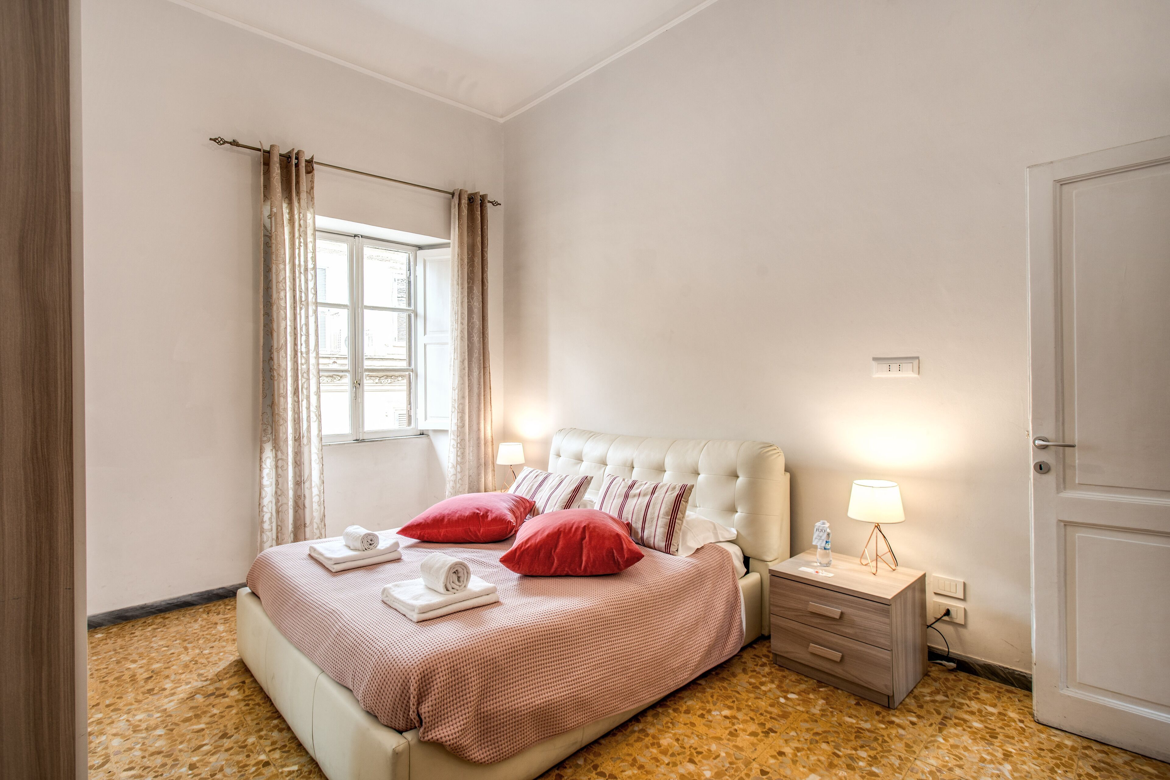 A bedroom with a bed, nightstands, a lamp, and a window with curtains.