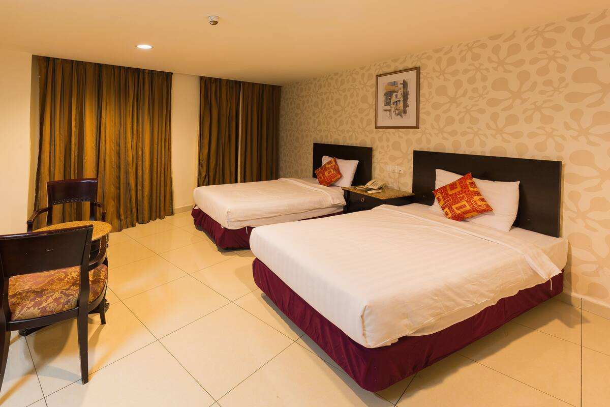 A hotel room with two beds, a chair, a nightstand, and a curtain.