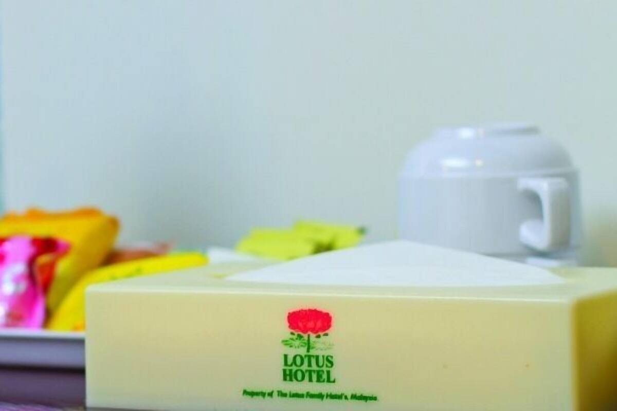 A hotel room with a bed, a bedside table, a water bottle, a mug, and a box of tissues.