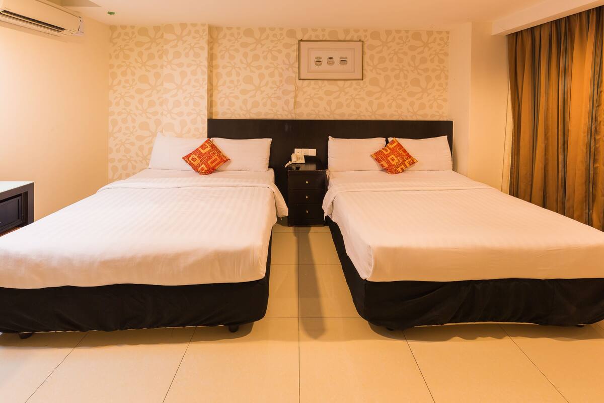 A hotel room with two beds, a nightstand, and a wall-mounted light switch.