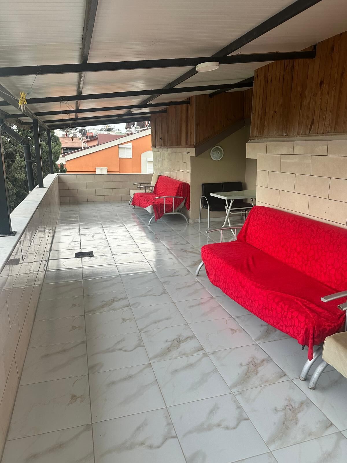 A covered outdoor seating area with tiled flooring, a red sofa, and a table.