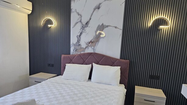 Ein modernes Schlafzimmer mit Marmorwand, einem gesteppten Kopfteil, einer karierten Bettdecke und zwei Nachttischen.