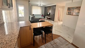 Eine moderne Küche mit Granit Arbeitsplatten, ein Essbereich mit Holztisch und -stühlen, ein Wohnzimmer mit Sofa und Fernseher sowie ein Flur mit einem Gemälde.
