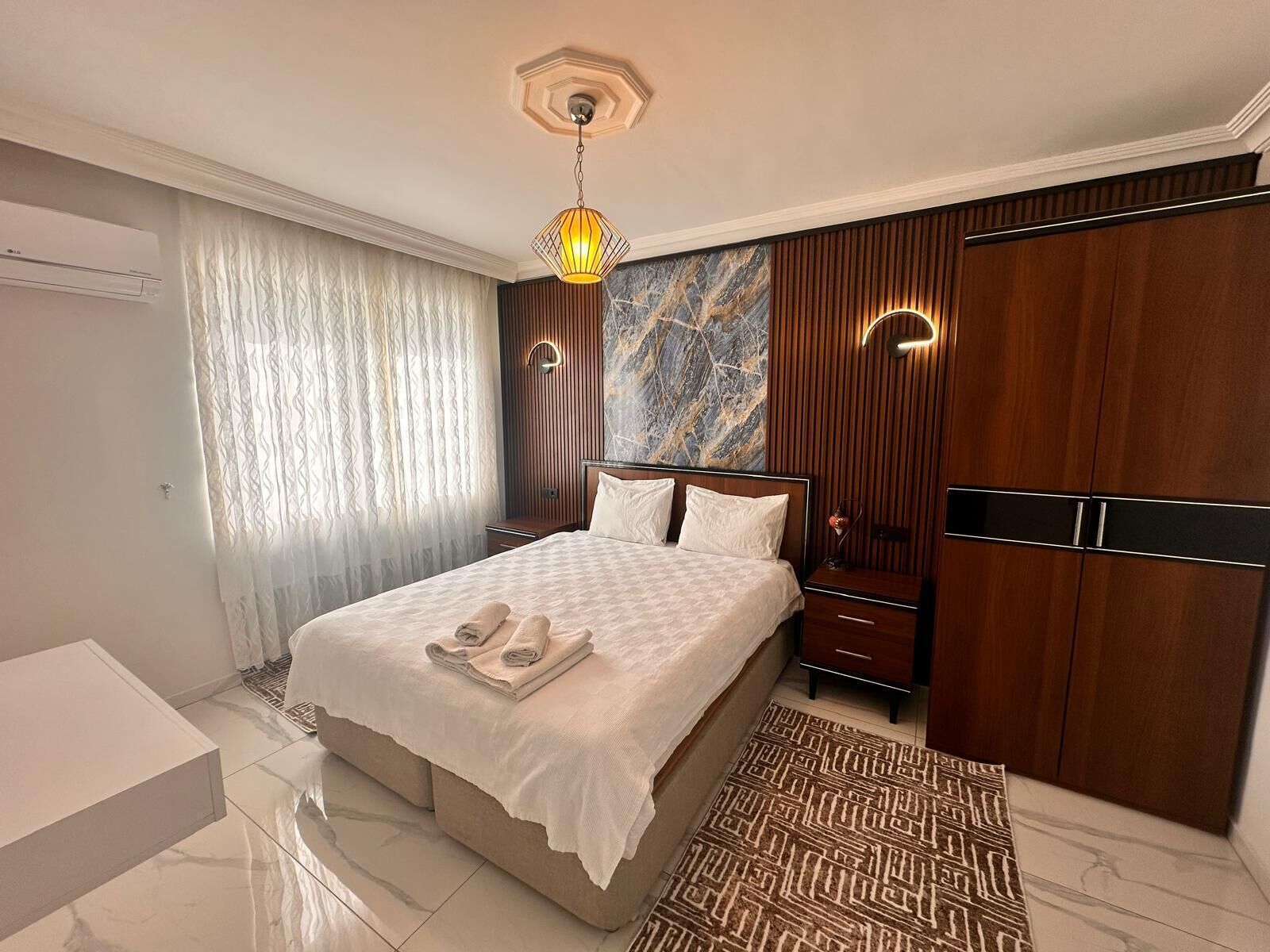 A hotel room with a bed, a bedside table, a wardrobe, a bathroom, and a marble floor.
