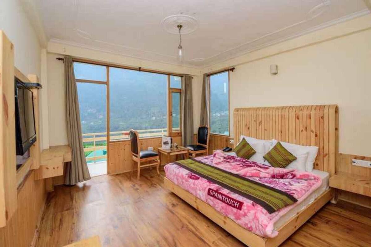 A bedroom with a bed, a desk, a chair, and large windows.