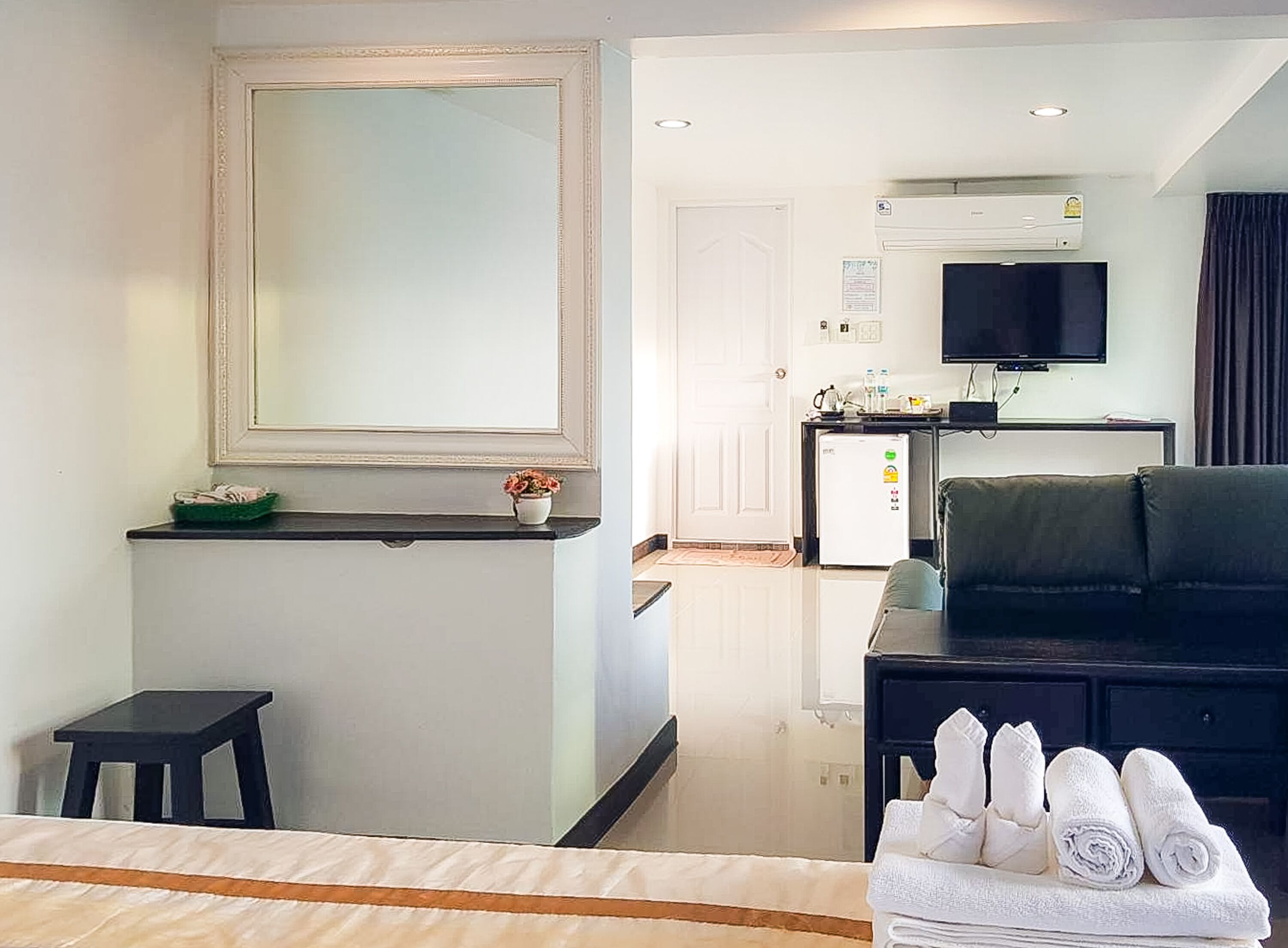 A hotel room with a bed, a desk, a chair, a TV, and a kitchenette.