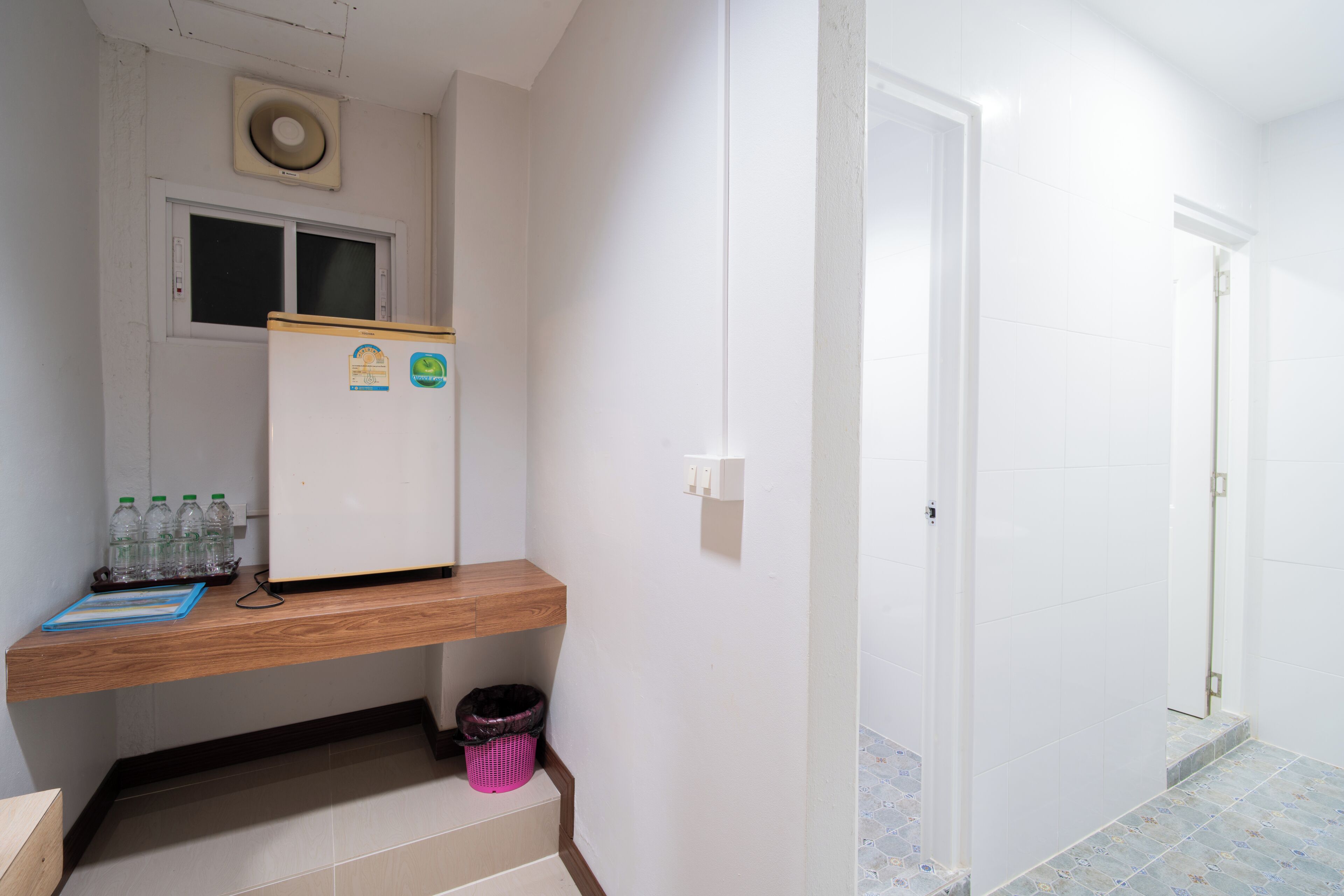 A small kitchenette with a refrigerator, a window, and a shelf with bottled water.
