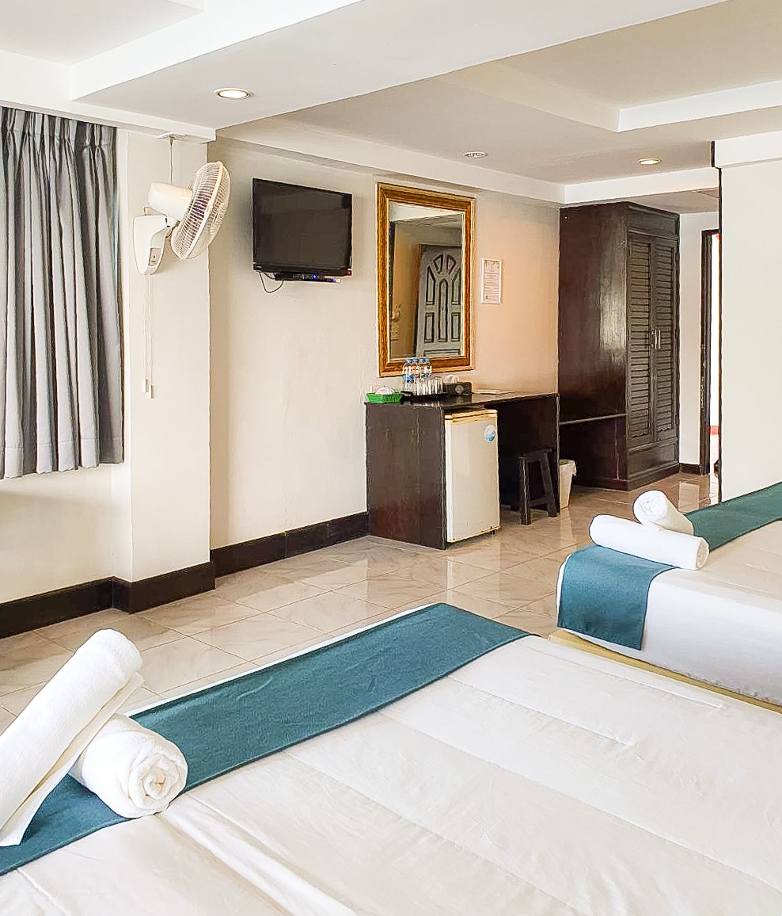 Habitación de hotel con dos camas, un escritorio, un espejo y un televisor.