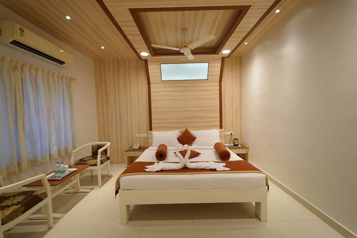 A hotel room with a bed, a desk, a chair, an air conditioning unit, a ceiling fan, and a television.