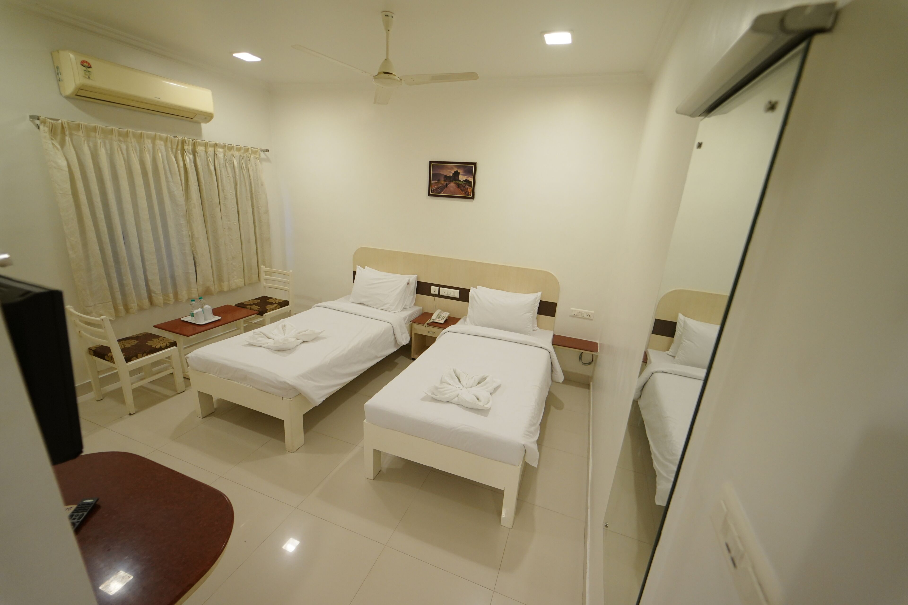 A hotel room with two beds, a desk, a chair, an air conditioner, a ceiling fan, and a small picture on the wall.