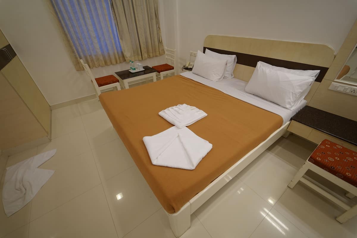 A hotel room with a bed, a bedside table, a chair, and a window with curtains.