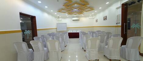 A conference room with rows of white chairs, a whiteboard, and a table with water bottles.
