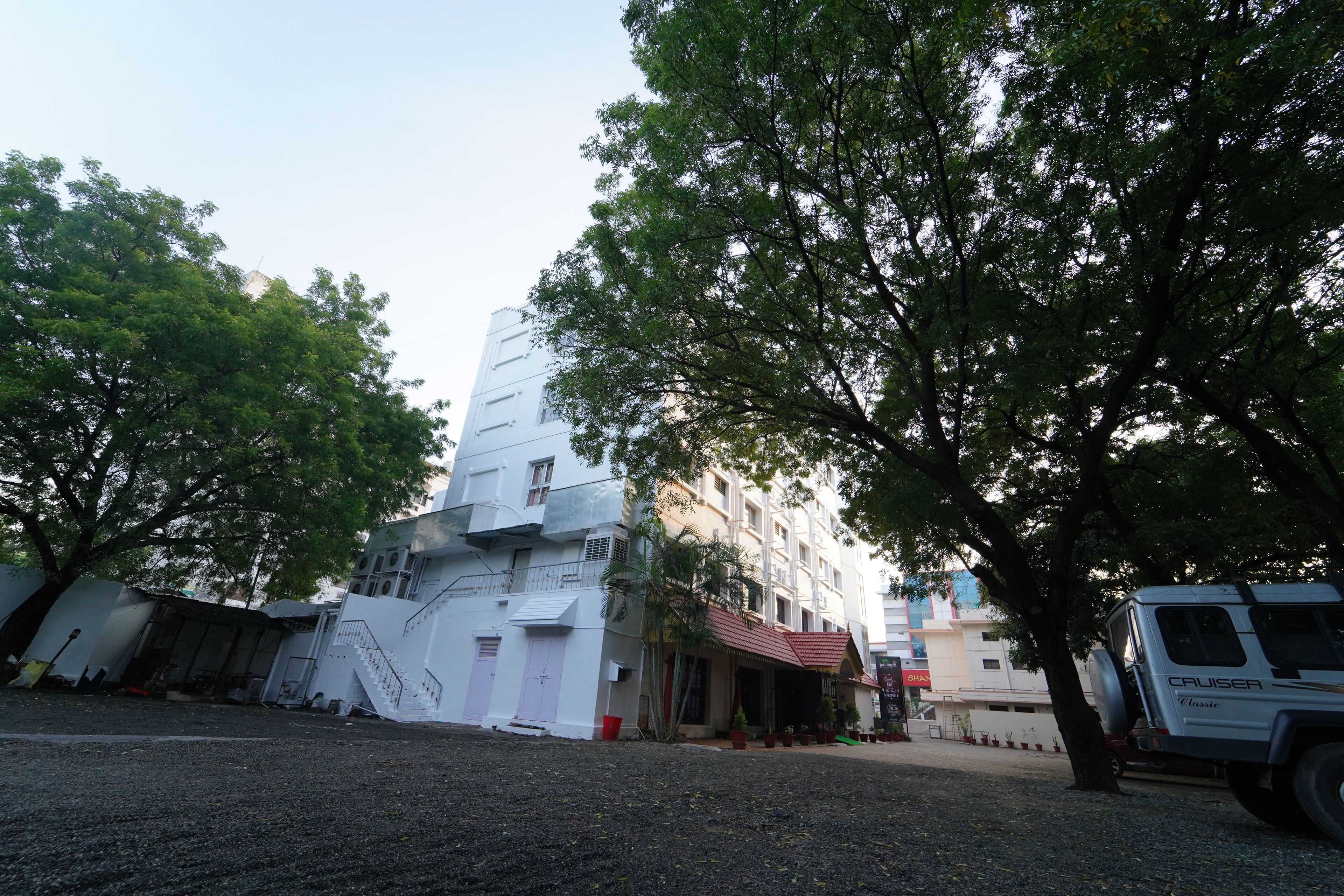 A multi-story building with a white facade, a red-roofed entrance, and a parked SUV.