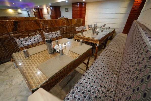 Un restaurante con cabinas de madera, cojines estampados y suelo de baldosas. Las mesas están preparadas con jarrones y vasos de metal.