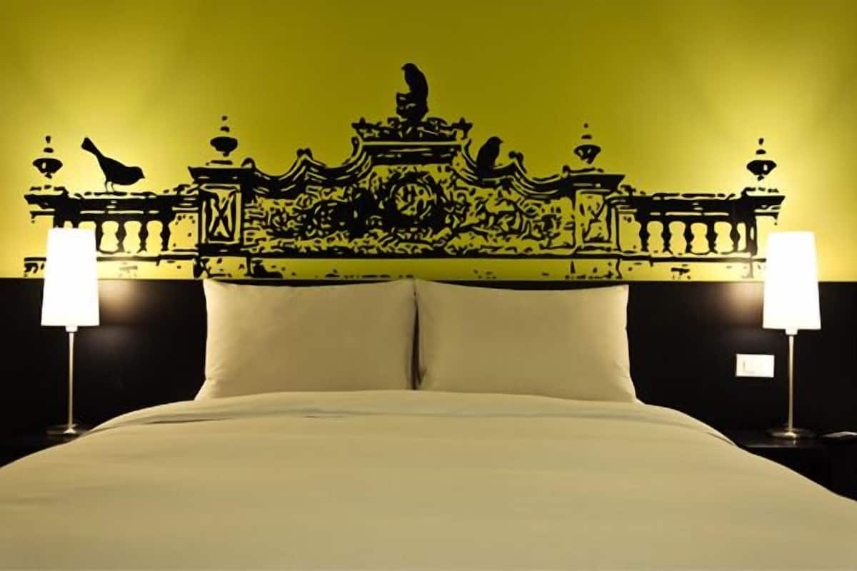 Ein Bett mit einem verzierten Kopfteil, zwei Nachttischlampen und einer schlichten Wand.
