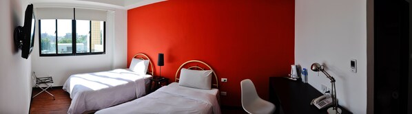 Habitación de hotel con dos camas, una pared de acento roja, una ventana con vistas, un escritorio con teléfono y una silla.