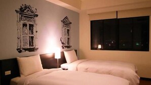 Ein Hotelzimmer mit zwei Betten, einem Nachttisch, einer Lampe und einem Fenster mit Blick auf die nächtliche Stadt.