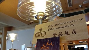 Ein Hotelrezeptionsschalter mit einem Holzschild, das den Hotelnamen, die Kontaktnummer und die Verfügbarkeit von WLAN anzeigt.