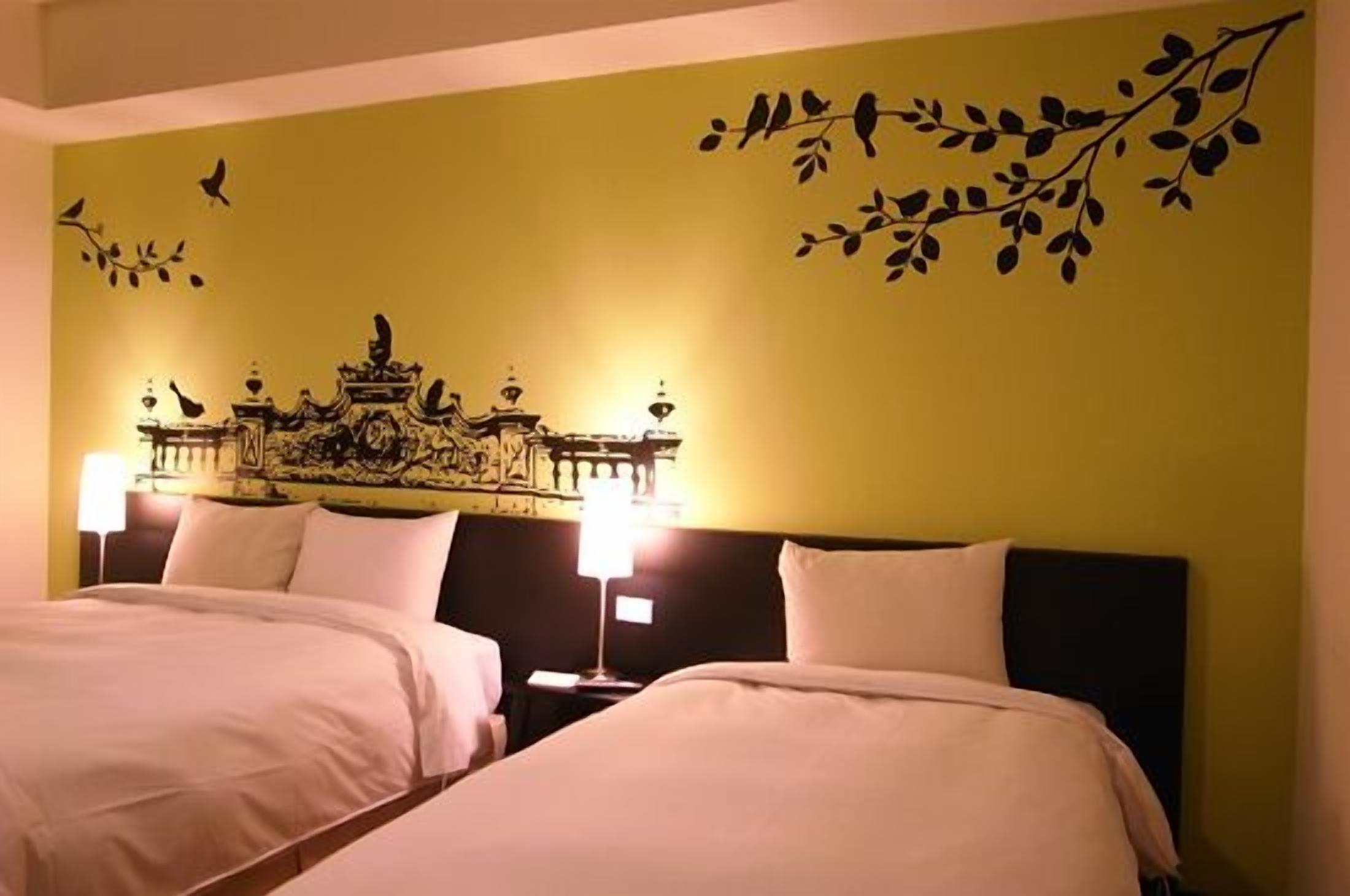 Quarto de hotel com duas camas, um mural decorativo e duas luminárias de cabeceira.