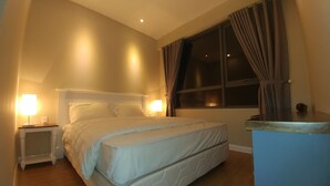 A neatly made bed in a hotel room with a headboard, two bedside lamps, a window with curtains, and a small wooden nightstand. - Cyber Masteri Thao Dien Apartment (Ho Chi Minh City)