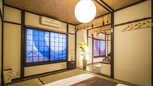 A traditional Japanese-style room with tatami flooring, a large window with a view of the sea, a hanging light fixture, and a small potted plant. - Kyo Oyado Hana (Kyoto)
