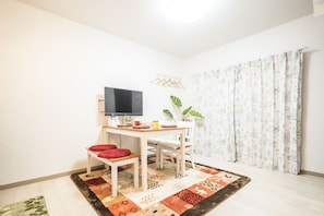 A small, bright room with a TV, a table, and a chair. There is a patterned rug on the floor and a curtain with a cityscape design. - Kyo Oyado Hana (Kyoto)