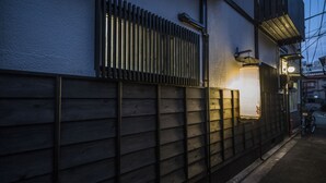 A narrow alleyway with a wooden fence, a bicycle, and a building with a slanted roof and a lit lantern. - Kyo Oyado Hana (Kyoto)
