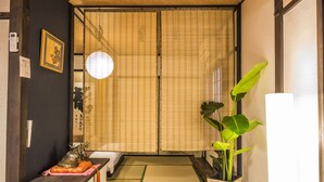 A traditional Japanese room with tatami flooring, a shoji screen door, a small table with a decorative item, a hanging light, and a potted plant. - Kyo Oyado Hana (Kyoto)