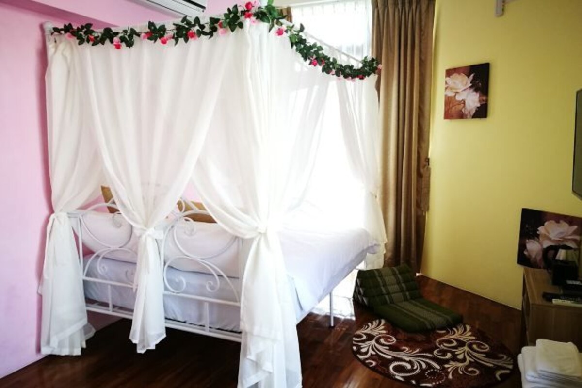 A room with a bed covered by a white canopy with floral decorations, a green chair, a patterned rug, and a painting on the wall.