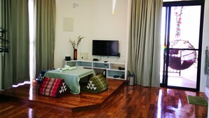 A living room with a wooden floor, a flat-screen TV, a sofa, and a coffee table. - 198 Red Hat B&B (Magong)