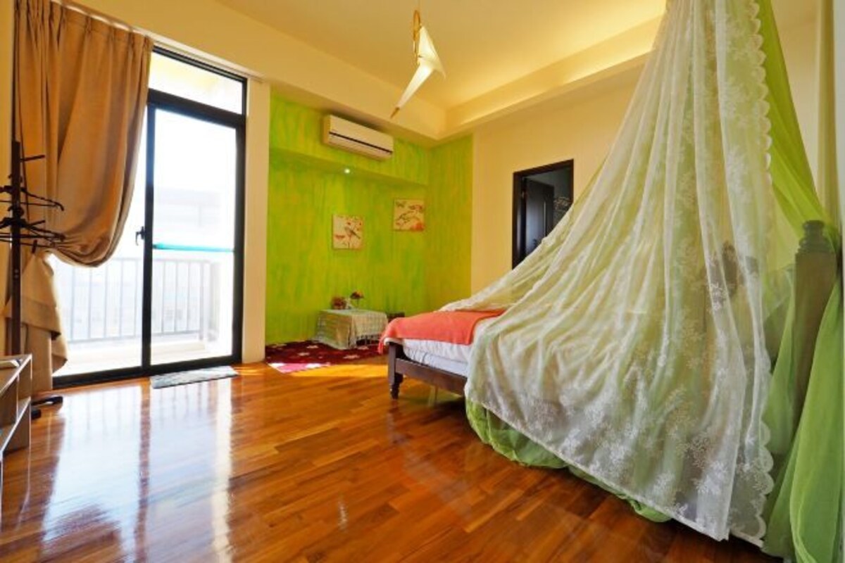 A bedroom with a bed, a window with curtains, a bedside table, and a green wall.