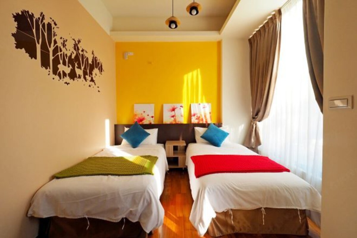 A hotel room with two single beds, a yellow accent wall, and a window with curtains.