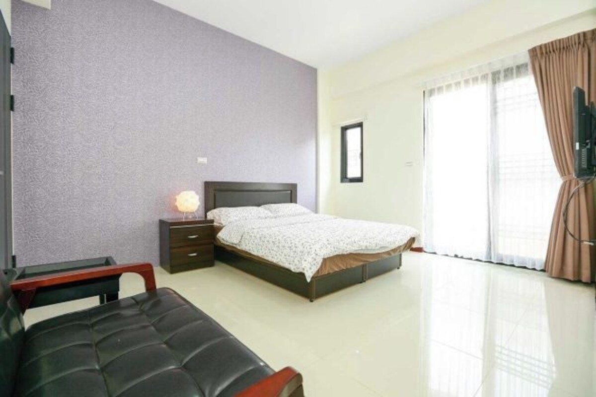 A bedroom with a bed, bedside table, lamp, and a TV on a stand.