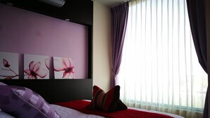 A bedroom with a bed, purple and red bedding, a wall-mounted air conditioner, and a window with sheer curtains. - 198 Red Hat B&B (Magong)