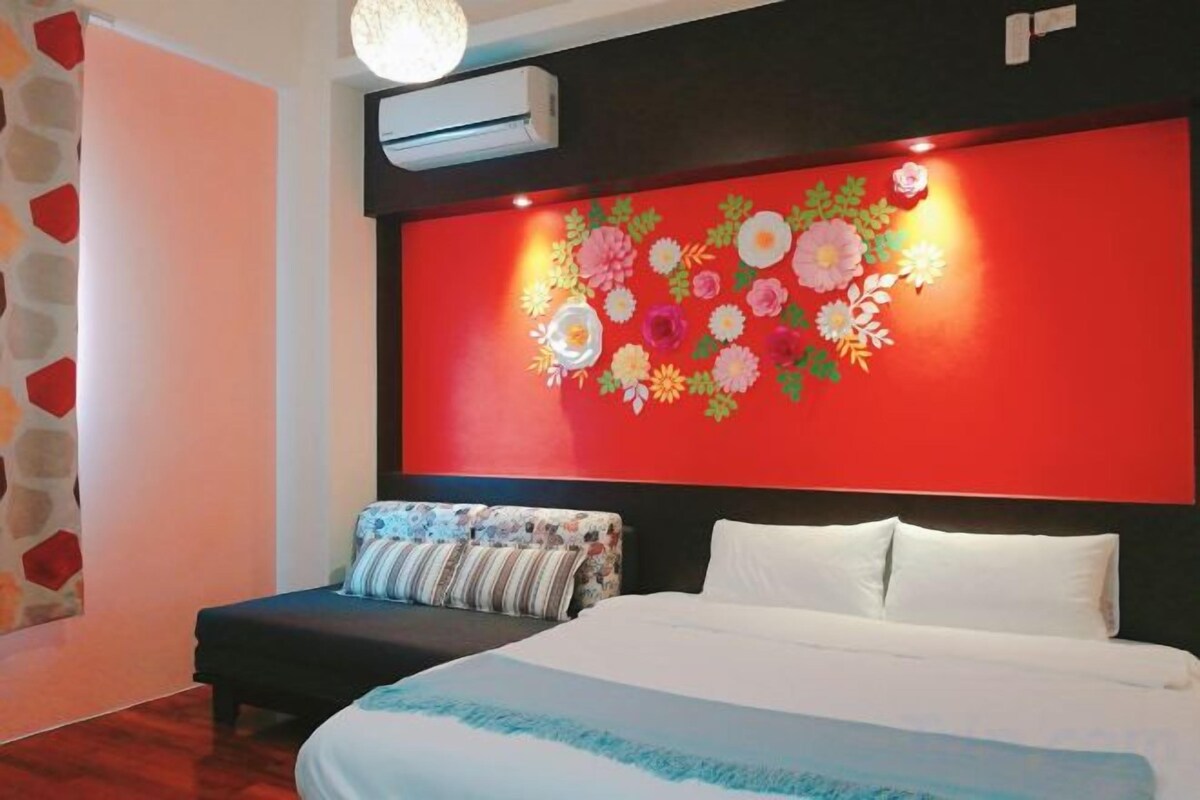 Une chambre d’hôtel avec un lit, un mur rouge orné de motifs floraux, une tête de lit noire et un oreiller blanc.