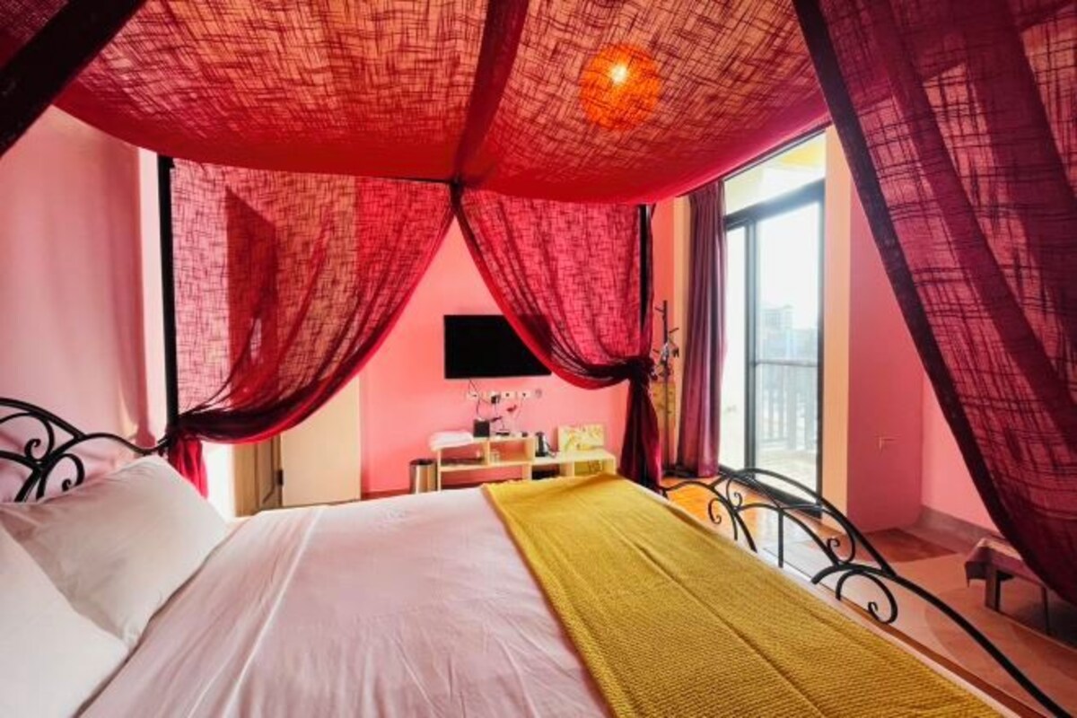 A bedroom with a bed, a bedside table, a window, and a curtain.