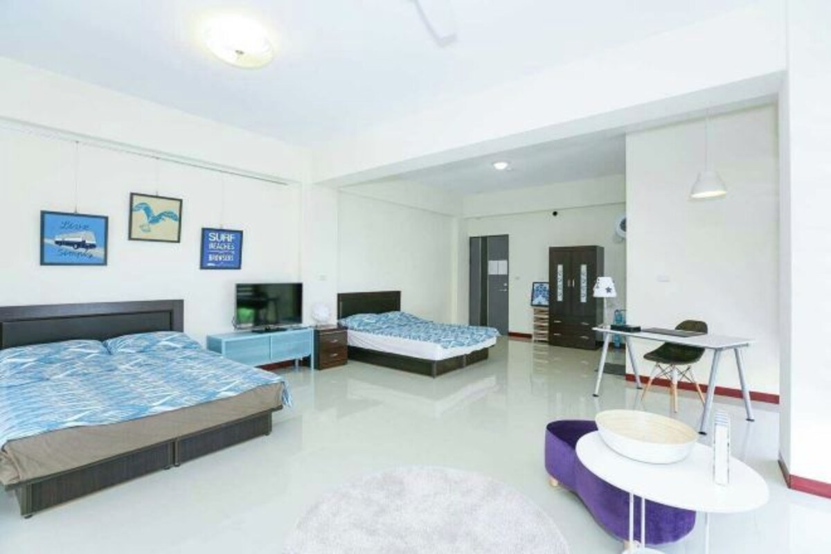 A modern bedroom with two beds, a TV, a desk, and a dining area.