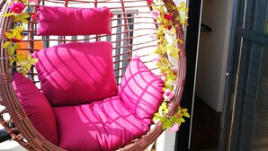A wicker hanging chair with pink cushions and a floral arrangement above it. - 198 Red Hat B&B (Magong)